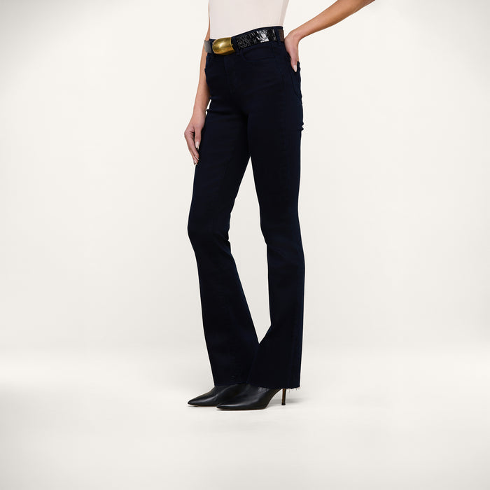 A person wearing Ruth Straight-Leg Jeans in an ultra dark indigo wash, a white top, a black belt with a gold buckle, and black heeled boots stands against a plain white background. Only the lower half of the body is visible.