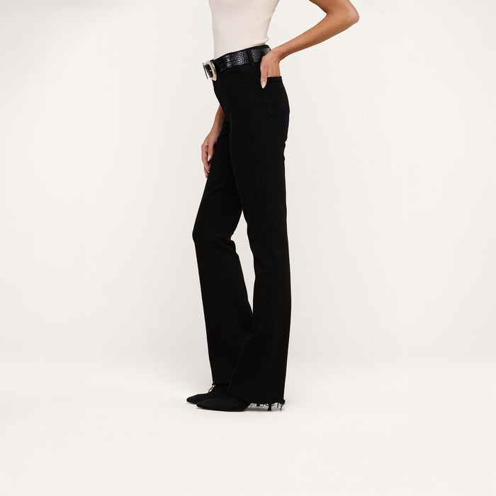 Woman wearing a sleeveless top, Ruth Straight-Leg Jean in black high-rise stretch denim, a black belt with a large buckle, and black shoes, standing against a plain white background.