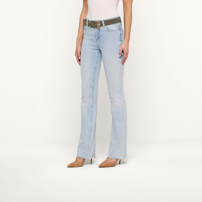 A woman wearing the Ruth Straight-Leg Jean in light blue with a raw hem, paired with a white sleeveless top, brown pointed-toe heels, and a camouflage belt, stands against a plain white background. Her head is not visible in the image.