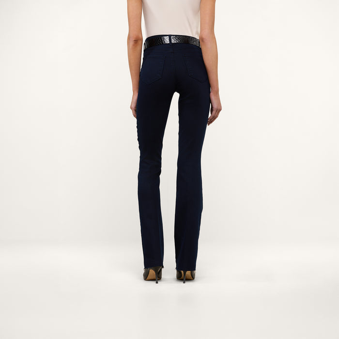 A person stands facing away, wearing a white sleeveless top, the Ruth Straight-Leg Jean in an ultra dark indigo wash, a black belt, and tan heels against a plain white background.