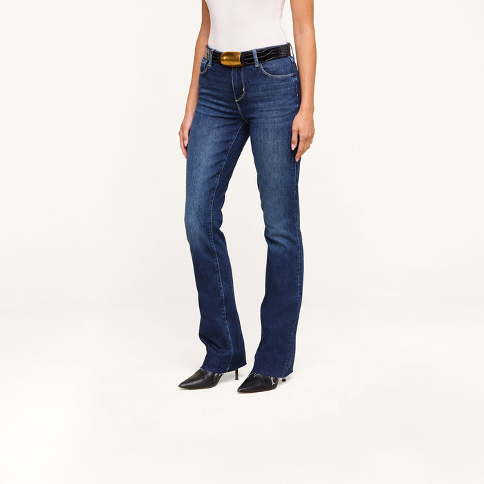 A person wearing Ruth Straight-Leg Jeans in dark blue, paired with a black belt featuring a gold buckle, black pointed shoes, and a white top stands against a plain white background.