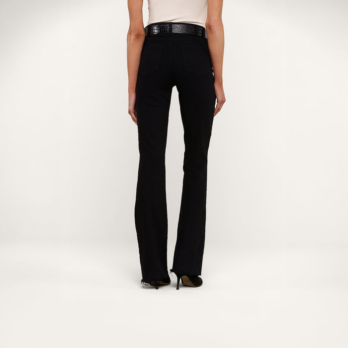 A person wearing the Ruth Straight-Leg Jean in black stretch denim, paired with a white top and black heels, stands facing away from the camera against a plain white background.