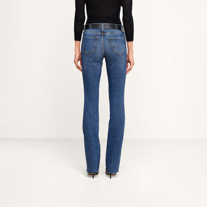 A person is shown from the back against a plain background, wearing a black long-sleeve top, black heels, and the Ruth Straight-Leg Jean in medium indigo wash with a fitted silhouette made from stretch denim.