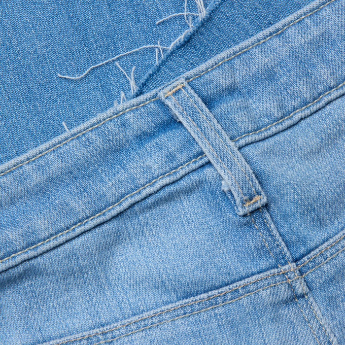 Close-up of the Ruth Straight-Leg Jean in light blue denim with a raw hem, featuring a visible belt loop, defined waistband, pocket stitching, and loose threads that accentuate the fabric’s texture and intricate details.