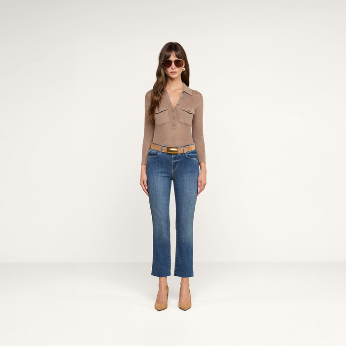 A woman wearing a brown long-sleeve top, tan belt, tan heels, sunglasses, and the Sada Cropped Slim-Leg Jean stands against a plain white background.