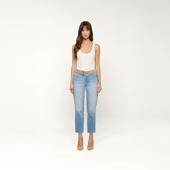 A woman stands facing forward against a plain white background wearing a white tank top, beige belt, beige heels, and the Sada Cropped Slim-Leg Jean in a light wash.