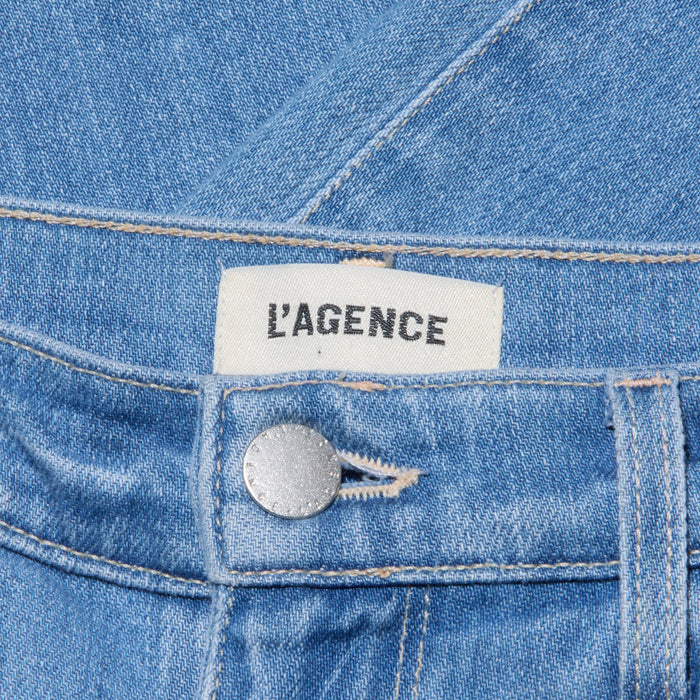 Close-up of light wash denim jeans showcasing a silver button, precise waistband stitching, and a white label with black text reading LAGENCE. The Sada Cropped Slim-Leg Jean features meticulous detailing and a modern silhouette.
