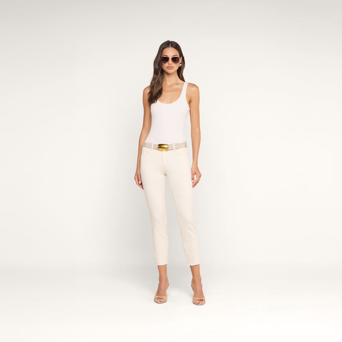 A woman in sunglasses wears a white tank top, beige belt, and the Sada Slim-Leg Cropped Jean—a cream high-rise jean with a slim straight leg fit—paired with beige high-heeled sandals, standing against a plain white background.