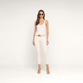 A woman in sunglasses wears a white tank top, beige belt, and the Sada Slim-Leg Cropped Jean—a cream high-rise jean with a slim straight leg fit—paired with beige high-heeled sandals, standing against a plain white background.