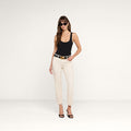 A woman wearing sunglasses, a black tank top, the Sada Slim-Leg Cropped Jean in high-rise white stretch denim, a black belt, and black heels stands against a plain white background.