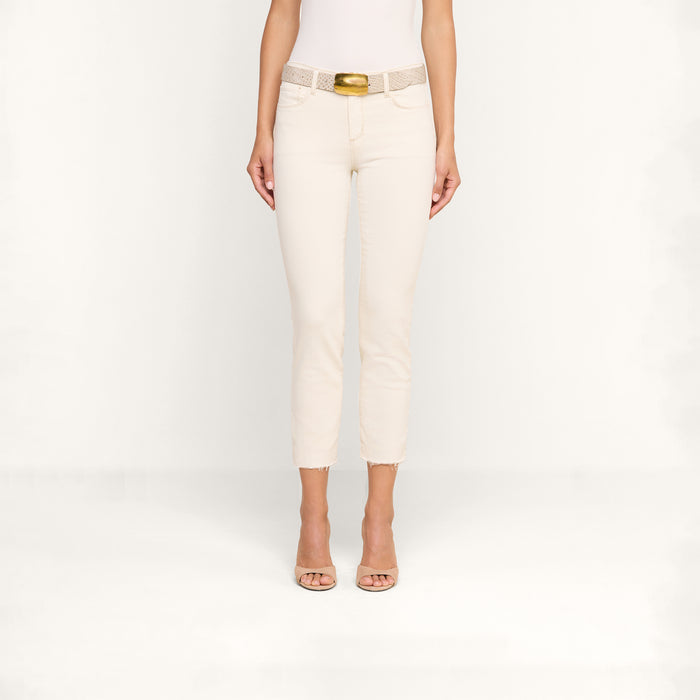 A person wearing the Sada Slim-Leg Cropped Jean in light beige, paired with a white top, a beige belt with a gold buckle, and beige open-toe heels stands against a plain white background.