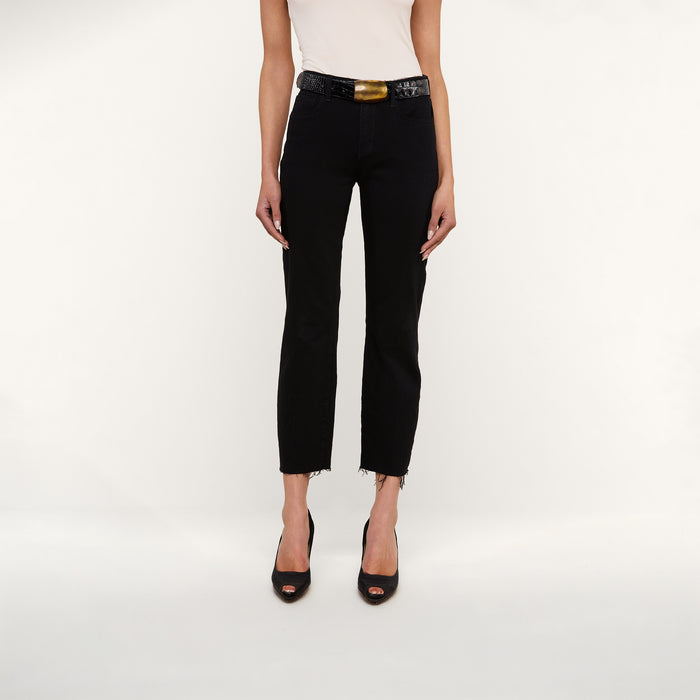 A person stands against a white background, wearing a sleeveless white top and Sada Slim-Leg Cropped Jeans with frayed hems, styled with a black belt featuring a gold buckle and black open-toe heels. Only the body below the shoulders is visible.