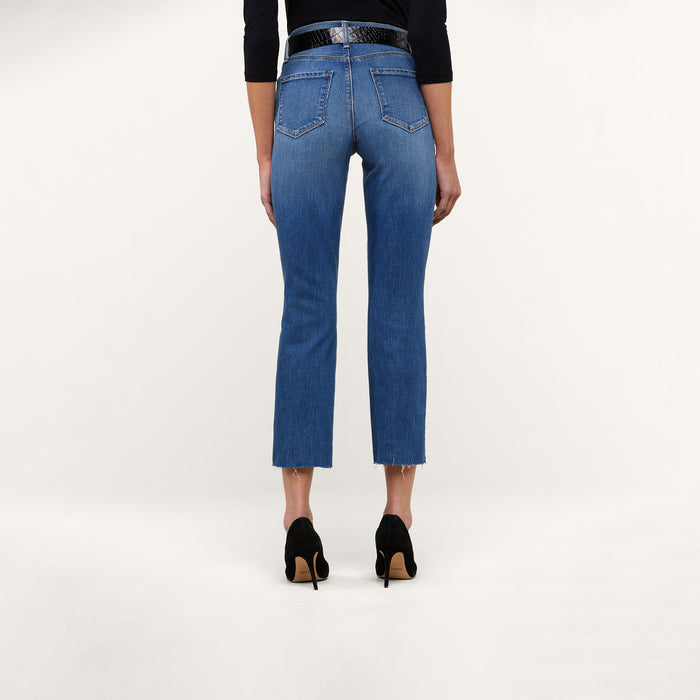A person stands with their back to the camera against a plain white background, wearing the Sada Slim-Leg Cropped Jean in premium stretch denim with frayed hems, paired with a black belt and black high-heeled shoes.