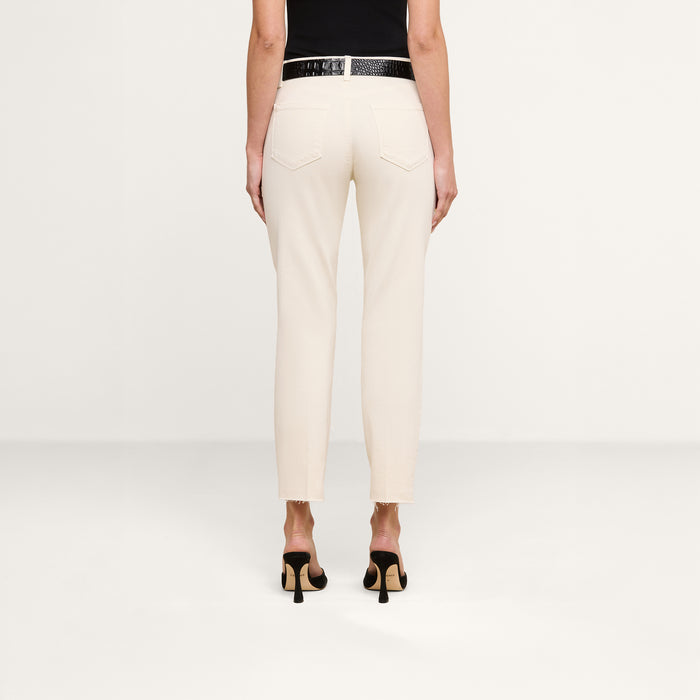 Person standing against a plain background, shown from the back. They are wearing the cream-colored Sada Slim-Leg Cropped Jean, a black belt, black top, and black heeled shoes.