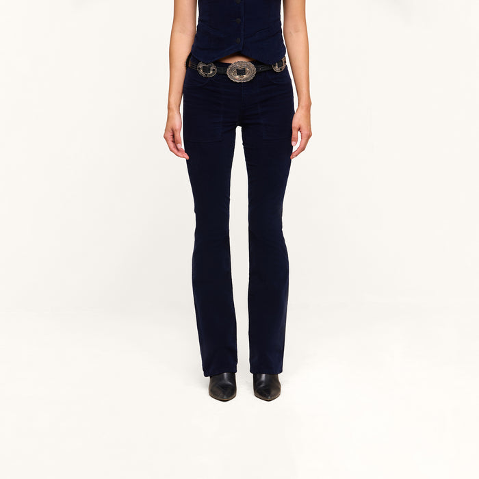 A person wearing the Saffia Corduroy Pant in dark blue, paired with a matching vest, wide belt, and black shoes stands against a plain white background. Their face is not visible.