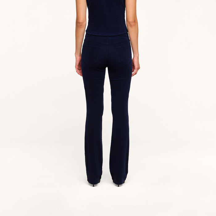 A person stands facing away from the camera, wearing a navy blue sleeveless top and the Saffia Corduroy Pant in a high-rise, flared silhouette, against a plain white background.