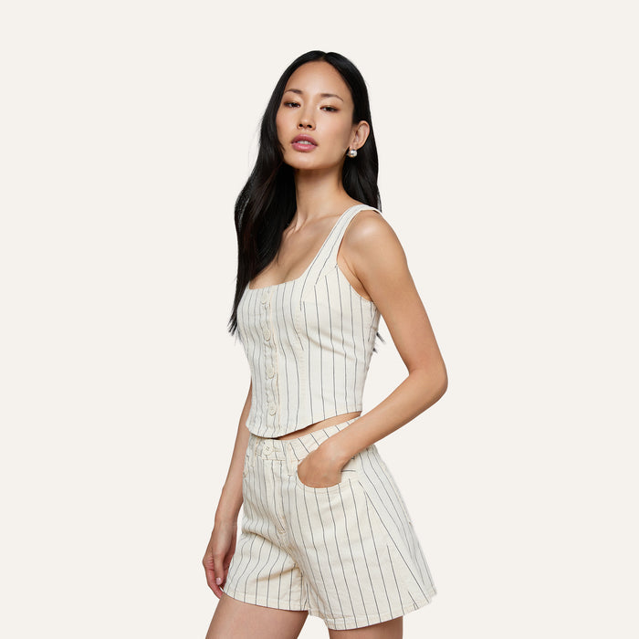 A woman wearing the sleeveless cream Saga Top with nautical stripes and matching shorts stands with one hand in her pocket against a plain light background.