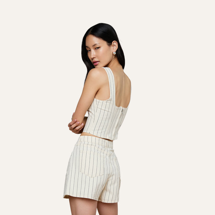 A woman models the sleeveless Saga Top, featuring subtle nautical stripes in a cream hue, paired with matching high-waisted cotton twill shorts as she stands against a plain light background.