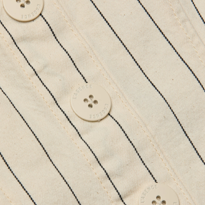 Close-up of the Saga Top, showcasing its off-white cotton twill fabric with thin black nautical stripes and four round buttons, each featuring four holes and text around the edges.
