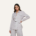 A woman poses with one hand on her hip against a plain background, wearing the Samaya Linen Jacket—a light-colored modern utility style featuring front pockets—paired with matching pants.