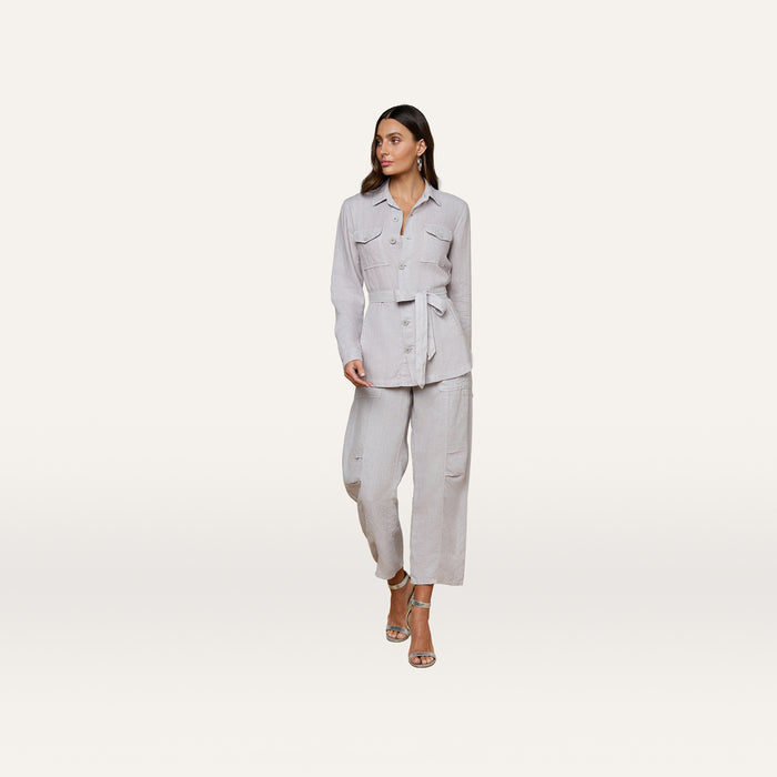 Wearing the Samaya Linen Jacket in light grey with a belt, this woman pairs it with matching straight-leg pants and heeled sandals as she walks against a plain white background.