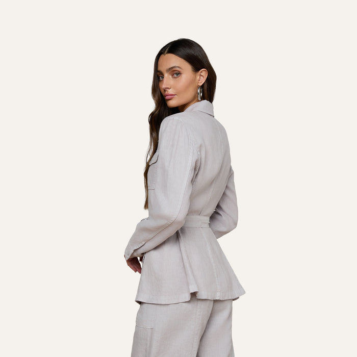 A woman with long brown hair wears the Samaya Linen Jacket and matching pants, posing with her body turned to the side and looking over her shoulder against a plain background.