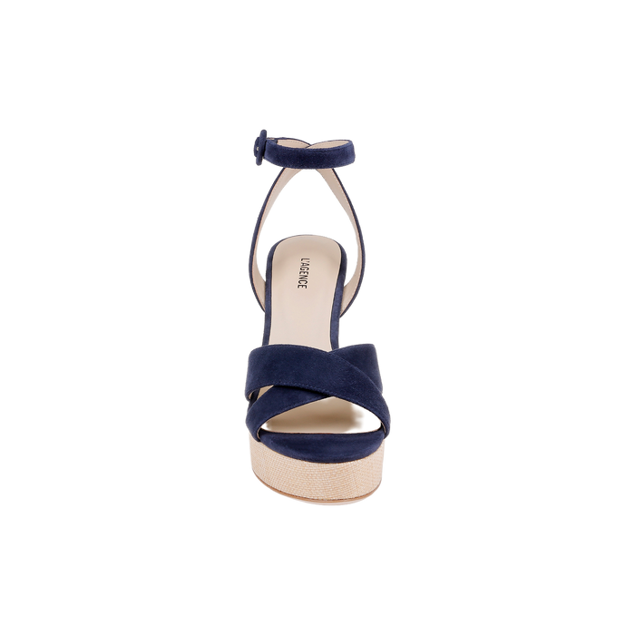 Front view of the Sandrine Platform Sandal, featuring navy suede crisscross straps over the toes, an ankle strap with a buckle, and a beige raffia-wrapped wedge sole, displayed on a plain white background.