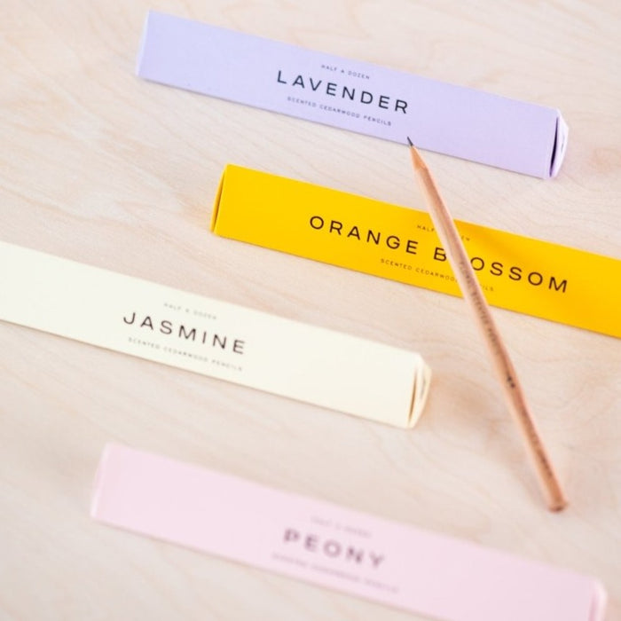 A scented pencil resting on the prism box packaging with the four different scents on display (top to bottom) Lavender, Orange Blossom, Jasmine and Peony