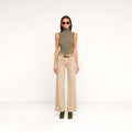 A woman in a sleeveless, olive-green turtleneck top, the Scottie Coated Wide-Leg Jean, green boots, and sunglasses stands against a plain white background.