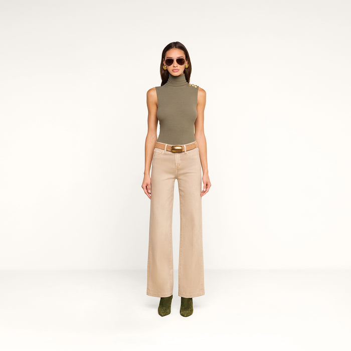 A woman in a sleeveless, olive-green turtleneck top, the Scottie Coated Wide-Leg Jean, green boots, and sunglasses stands against a plain white background.
