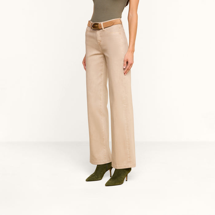 A woman models the Scottie Coated Wide-Leg Jean in beige, styled with a tan belt and green suede heeled boots, posing against a plain white background with only her torso and legs visible.