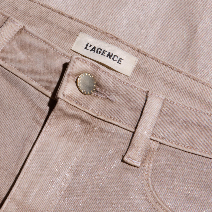 Close-up of the Scottie Coated Wide-Leg Jean in light pink, featuring a metallic button and a white L’AGENCE label sewn onto the waistband. The coated denim fabric gives off a subtle sheen, with visible stitching details.