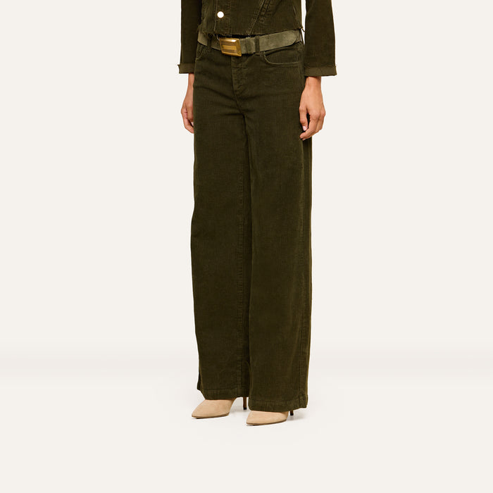 Wearing the Scottie Corduroy Pant—a high-waisted, wide-leg style in dark olive green with a matching belt—paired with beige pointed-toe heels, this look shown from shoulders down against a plain background highlights a chic fall 2026 fashion ensemble.
