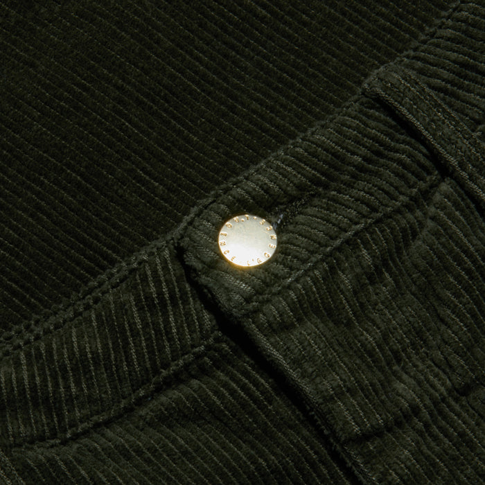 Close-up of the Scottie Corduroy Pant in dark green, featuring a high-rise, wide-leg silhouette with a metallic button at the waistband that highlights the fabric’s rich ribbed texture and detailed edging—an elevated choice for fall 2026 fashion.