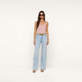 A woman stands against a plain white background wearing sunglasses, a pink tank top, brown shoes, and the Scottie Wide-Leg Jean in a light wash high-rise style with a belt.