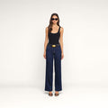 A woman wearing sunglasses, a black tank top, the Scottie Wide-Leg Jean in blue high-rise premium stretch denim with a large belt buckle, and black heels stands against a plain white background.