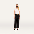 A woman with long blonde hair, wearing black sunglasses, a white short-sleeve top, and the Scottie Wide-Leg Jean paired with a black belt and black heels stands against a plain white background.