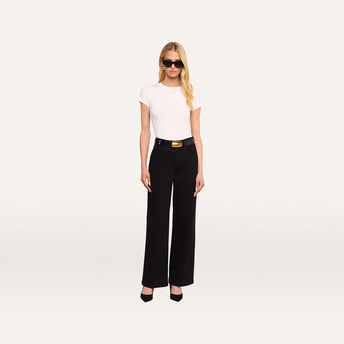 A woman with long blonde hair, wearing black sunglasses, a white short-sleeve top, and the Scottie Wide-Leg Jean paired with a black belt and black heels stands against a plain white background.