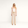 A person with long blonde hair wearing sunglasses, a sleeveless beige top, and the Scottie Wide-Leg Jean made from premium stretch denim with a belt and brown heels stands against a plain white background.