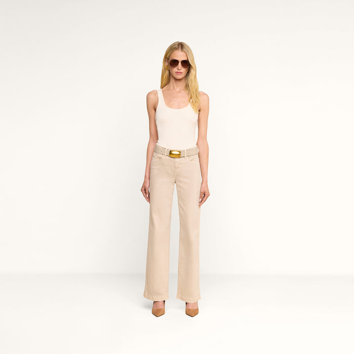 A person with long blonde hair wearing sunglasses, a sleeveless beige top, and the Scottie Wide-Leg Jean made from premium stretch denim with a belt and brown heels stands against a plain white background.