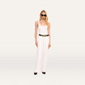 A woman wearing black sunglasses, a white tank top, the Scottie Wide-Leg Jean with a high-rise waistband, a black belt, black heels, and gold earrings stands against a plain, light background.