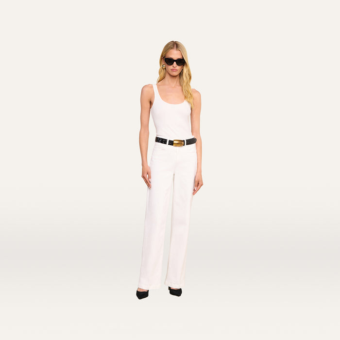 A woman wearing black sunglasses, a white tank top, the Scottie Wide-Leg Jean with a high-rise waistband, a black belt, black heels, and gold earrings stands against a plain, light background.