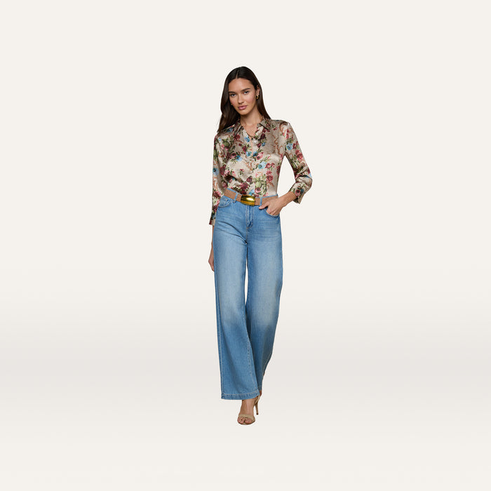 A woman wearing a floral long-sleeve blouse, the Scottie Wide-Leg Jean in a light wash with a contoured waistband, and beige heels stands against a plain white background.