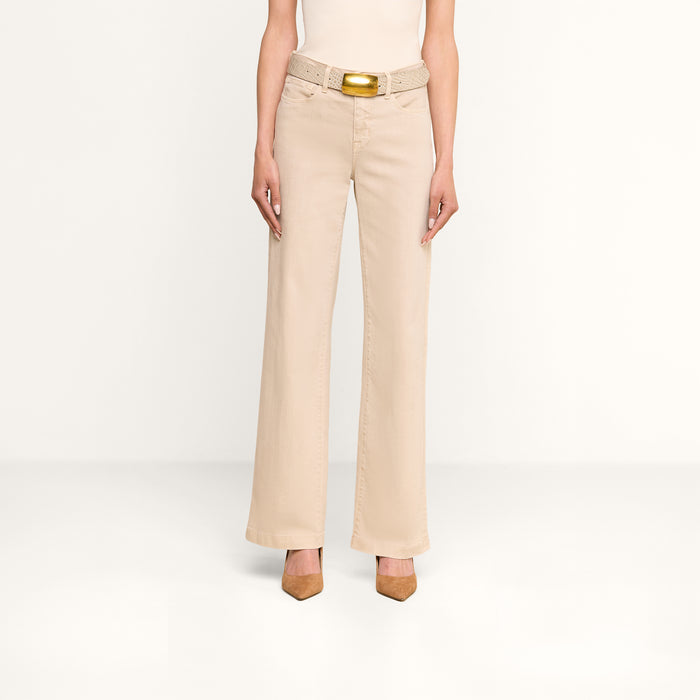 A person stands against a plain white background wearing the Scottie Wide-Leg Jean in beige, styled with a woven beige belt featuring a gold buckle and tan pointed-toe heels. The upper body is not visible.