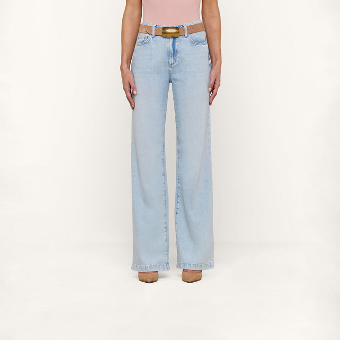 Wearing the Scottie Wide-Leg Jean in a light wash with a beige belt, a pink top, and tan shoes, the person stands against a plain white background.