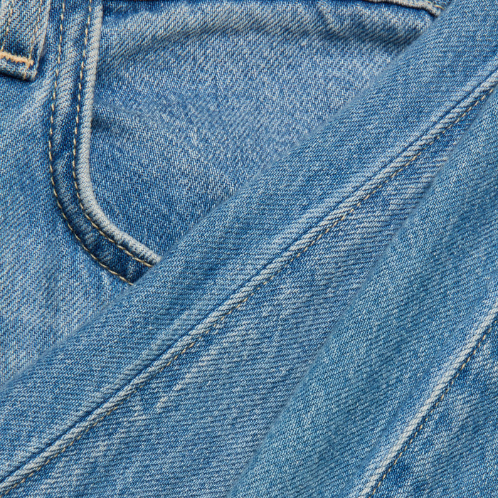 Close-up of the Scottie Wide-Leg Jean in blue denim, highlighting the stitching and a pocket, with another piece of light wash Scottie Wide-Leg Jean fabric laid diagonally across the image.