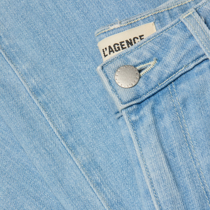Close-up photo of light blue stretch denim Scottie Wide-Leg Jean featuring a metal button and a visible white fabric label reading LAGENCE, partially tucked under the contoured waistband.