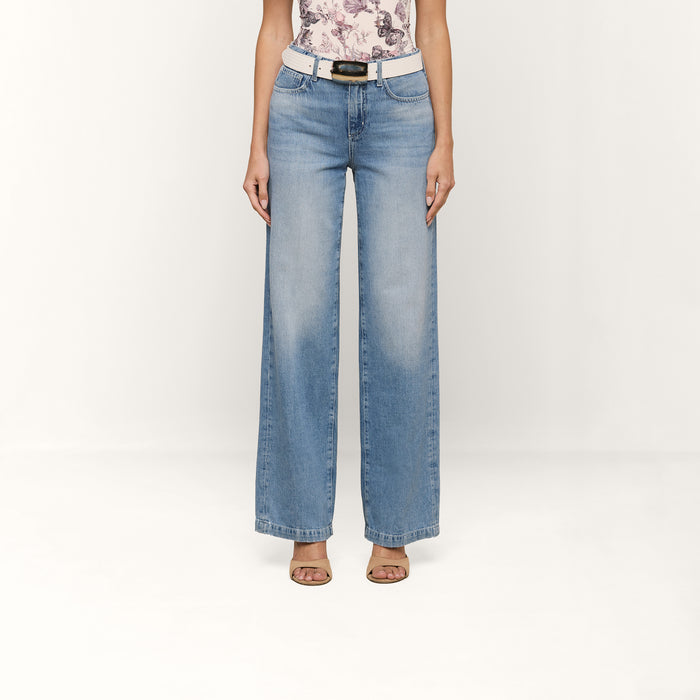Wearing the Scottie Wide-Leg Jean, a person stands against a plain white background, styled with a white belt, a floral top, and open-toe heels.