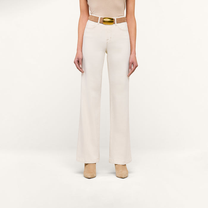 A person wearing the Scottie Wide-Leg Jean in an off-white wash, styled with a tan belt and beige shoes, stands against a plain white background. The upper body is mostly out of frame.