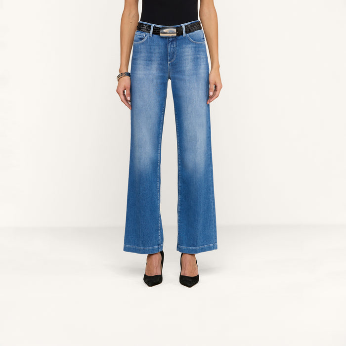 Wearing the Scottie Wide-Leg Jean, a person stands against a plain white background, styled with a black belt, black sleeveless top, black heels, and bracelets.